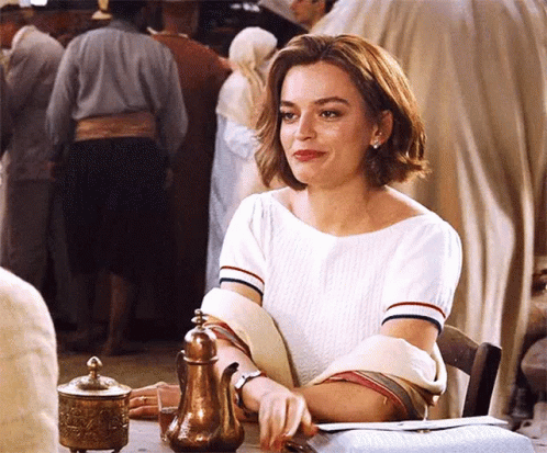 A Woman In A White Shirt Is Sitting At A Table With A Teapot In Front Of Her . GIF