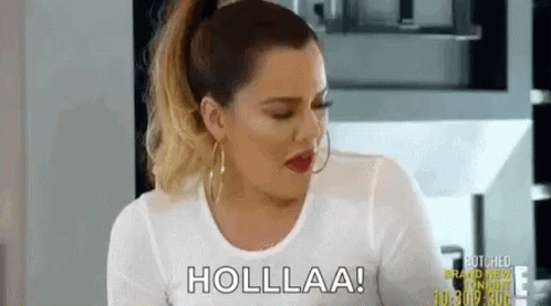A Woman In A White Shirt Is Sitting In A Kitchen Talking To Someone . GIF