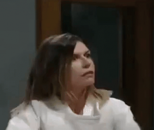 A Woman In A White Shirt Is Sitting In Front Of A Window And Looking At The Camera . GIF