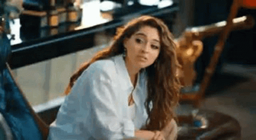A Woman In A White Shirt Is Sitting On A Chair In A Room . GIF