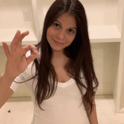 A Woman In A White Shirt Is Smiling And Holding Something In Her Hand GIF