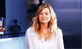 A Woman In A White Shirt Is Smiling And Looking At The Camera In A Kitchen . GIF