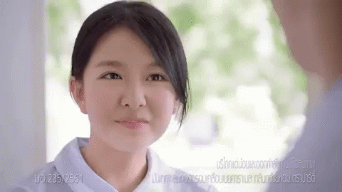 A Woman In A White Shirt Is Smiling In Front Of A Sign That Says 265/2561 GIF