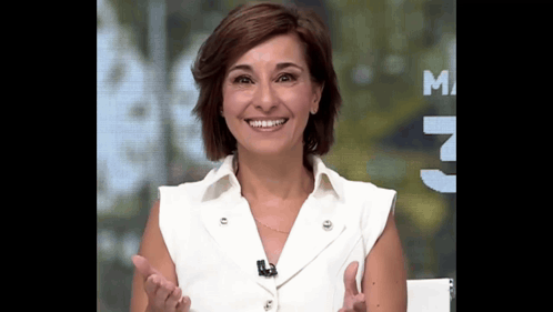 a woman in a white shirt is smiling in front of a sign that says m