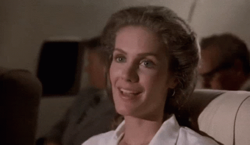 A Woman In A White Shirt Is Smiling While Sitting On A Plane GIF