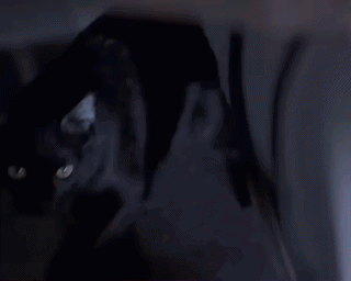 A Woman In A White Shirt Is Standing In A Dark Room . GIF