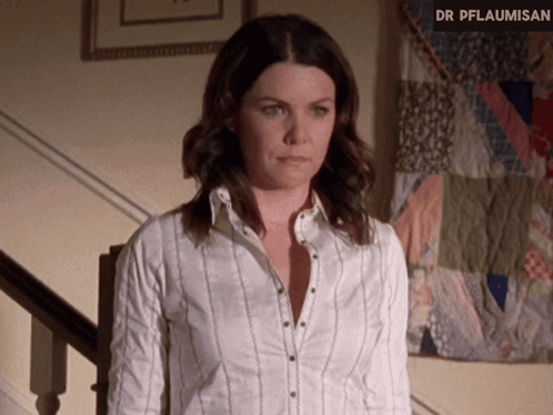 A Woman In A White Shirt Is Standing In Front Of A Quilt That Says Dr Pflaumisen GIF