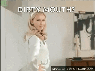 A Woman In A White Shirt Is Standing In Front Of A Wall With The Words `` Dirty Mouth '' Written On It . GIF