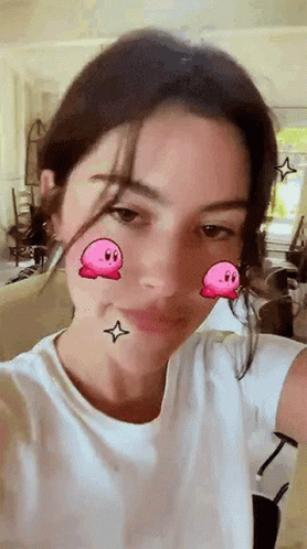 A Woman In A White Shirt Is Taking A Selfie With A Kirby Filter On Her Face . GIF