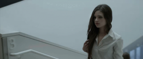 A Woman In A White Shirt Is Walking Down A Set Of Stairs With The Number 3 On The Wall Behind Her GIF