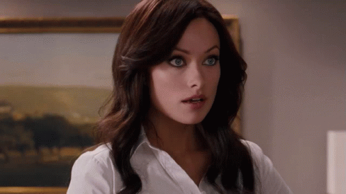 A Woman In A White Shirt Stands In Front Of A Framed Painting GIF