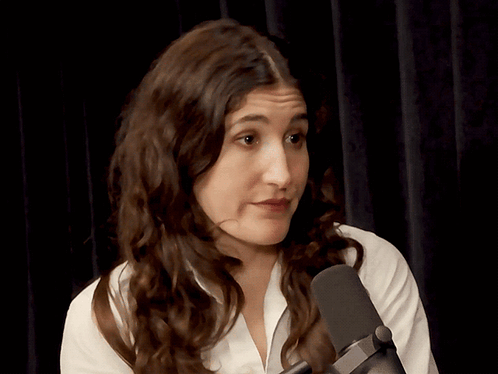 A Woman In A White Shirt Stands In Front Of A Microphone Making A Funny Face GIF