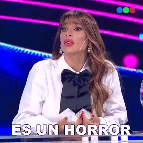 A Woman In A White Shirt With A Black Bow Tie Is Sitting At A Table Saying Es Un Horror GIF