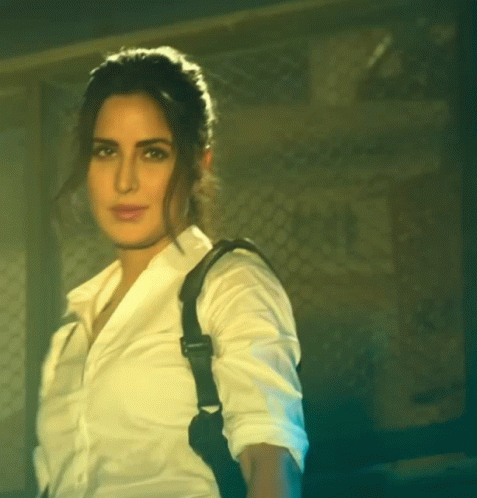 A Woman In A White Shirt With A Black Strap On Her Back GIF