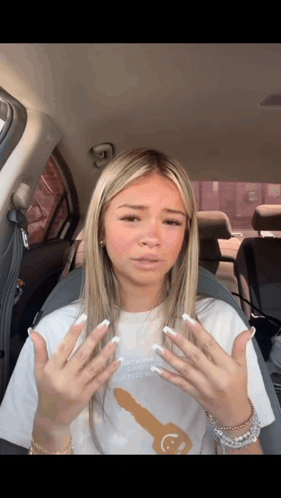 A Woman In A White Shirt With A Key On It Is Sitting In The Back Seat Of A Car GIF