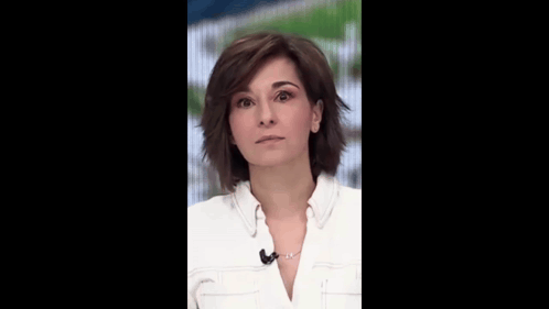 a woman in a white shirt with a microphone on her neck smiles