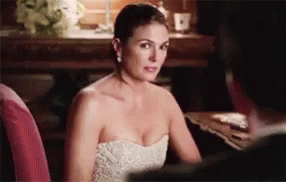 A Woman In A White Strapless Dress Is Sitting At A Table With A Man . GIF