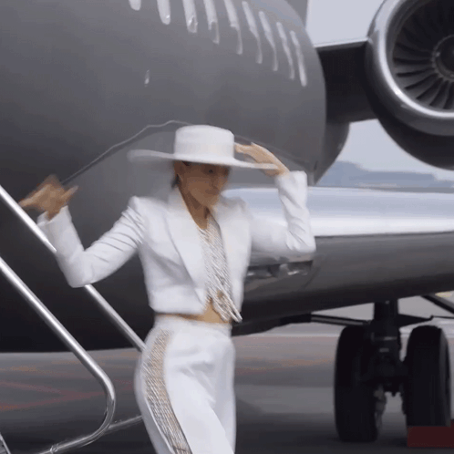 a woman in a white suit and hat is standing in front of a plane