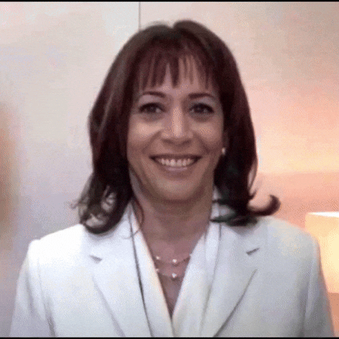 A Woman In A White Suit And Pearls Smiles For The Camera GIF