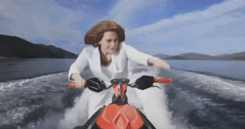 A Woman In A White Suit Is Riding A Jet Ski In The Water GIF