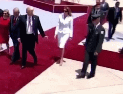 A Woman In A White Suit Is Walking On A Red Carpet With A Man In A Suit And Tie . GIF