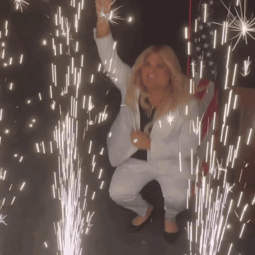 A Woman In A White Suit Stands In Front Of A Firework Display GIF