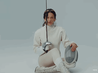 A Woman In A White Sweater Is Holding A Fencing Sword GIF