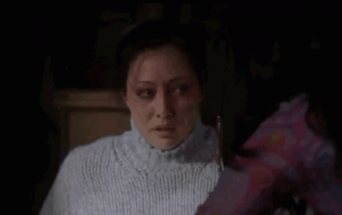 A Woman In A White Sweater Is Looking At Another Woman In A Purple Shirt In A Dark Room . GIF
