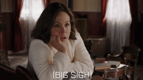 A Woman In A White Sweater Is Sitting In A Chair With Her Hand On Her Chin And The Words Big Sigh Below Her GIF