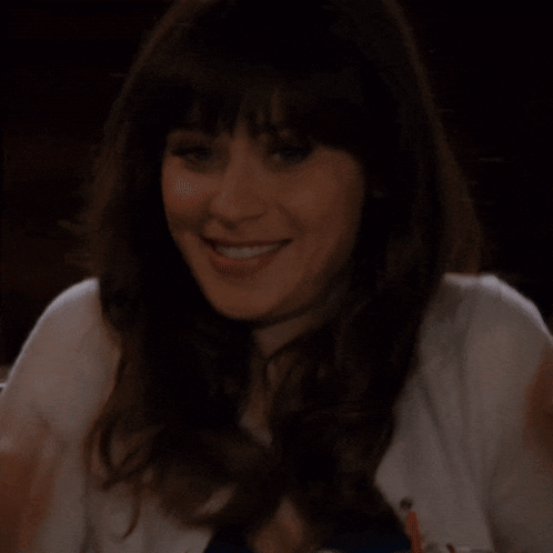 A Woman In A White Sweater Is Smiling With Her Hands On Her Chin GIF