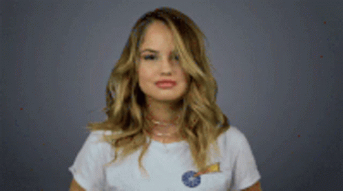 A Woman In A White T-Shirt Is Holding A Lollipop And Making A Funny Face . GIF