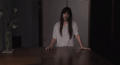 a woman in a white t-shirt is pointing at her chest