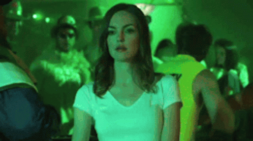 A Woman In A White T-Shirt Is Sitting In A Crowded Room . GIF