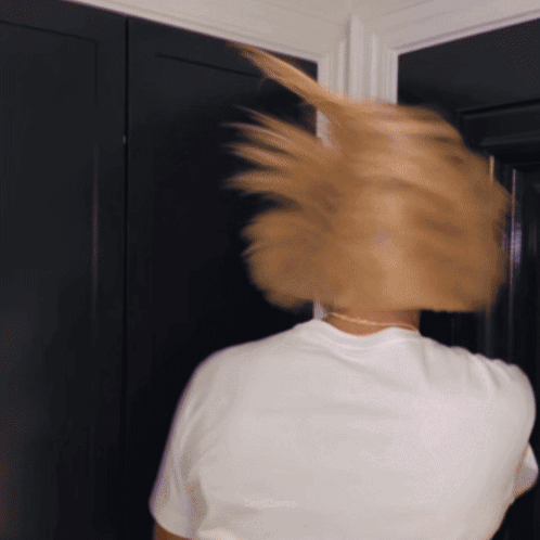 A Woman In A White T-Shirt Is Standing In Front Of A Door GIF