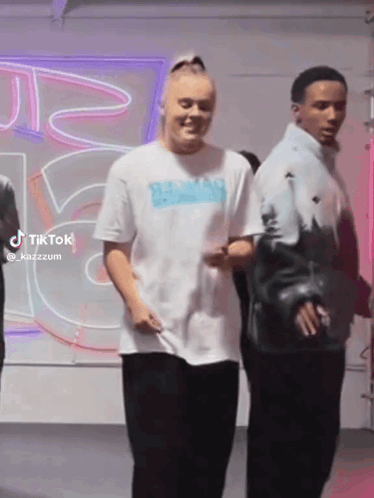 A Woman In A White T-Shirt Is Standing Next To A Man In A Blue Jacket . GIF