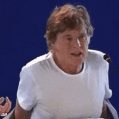 A Woman In A White T-Shirt Is Talking Into A Microphone GIF