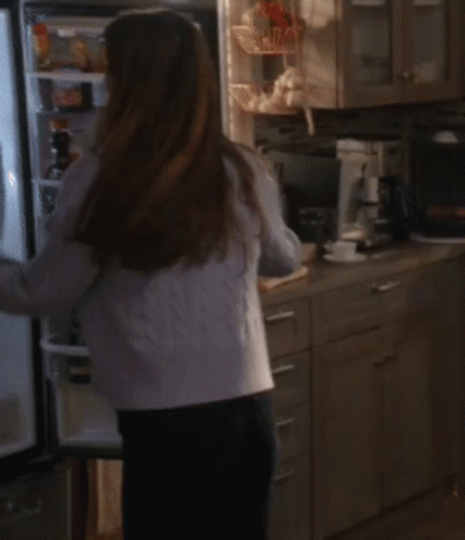 A Woman In A White Tank Top And A Blue Cardigan Is Dancing In The Kitchen GIF