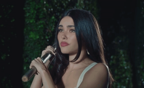 A Woman In A White Tank Top Holds A Microphone GIF