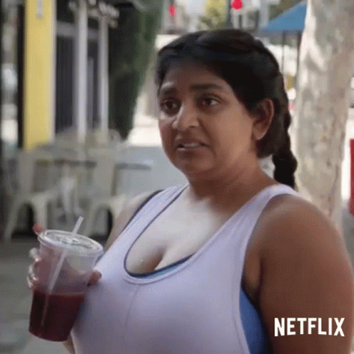 A Woman In A White Tank Top Is Holding A Cup With A Straw In Her Hand . GIF