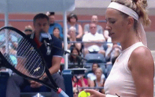 A Woman In A White Tank Top Is Holding A Tennis Racquet And A Ball . GIF