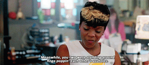 A Woman In A White Tank Top Is Standing In Front Of A Computer And Talking To Another Woman . GIF