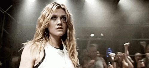 A Woman In A White Tank Top Is Standing In Front Of A Crowd Of People . GIF