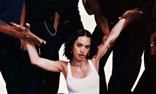 A Woman In A White Tank Top Is Surrounded By A Group Of People . GIF