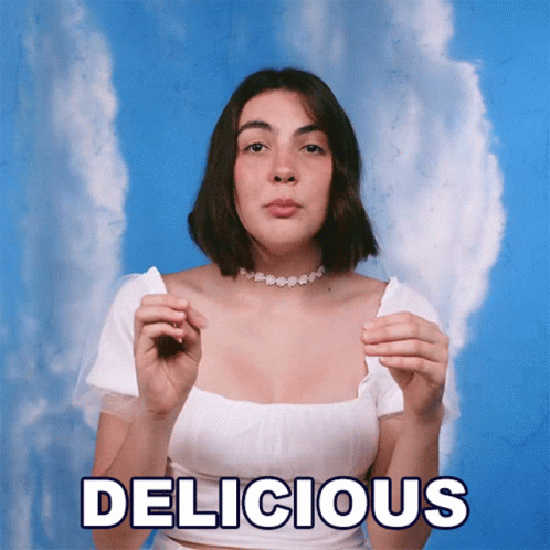 A Woman In A White Top Is Holding A Piece Of Paper With The Word Delicious Written On It GIF
