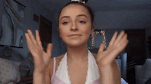 A Woman In A White Top Is Making A Face With Her Hands Outstretched GIF