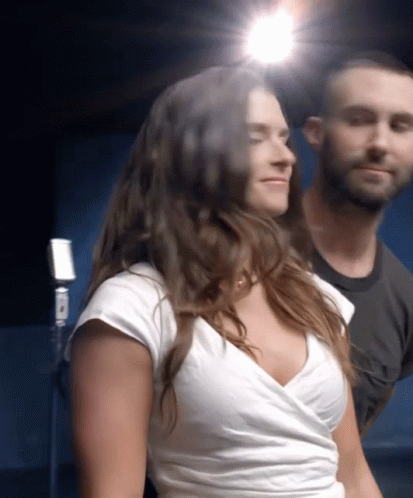 A Woman In A White Top Is Standing Next To A Man GIF