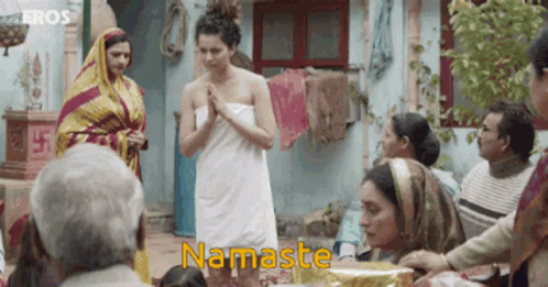 A Woman In A White Towel Is Praying In Front Of A Group Of People And The Word Namaste Is On The Bottom GIF
