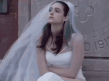 a woman in a white wedding dress and veil is sitting on a bed .