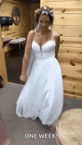 A Woman In A White Wedding Dress Is Dancing In A Room With A Wooden Wall . GIF