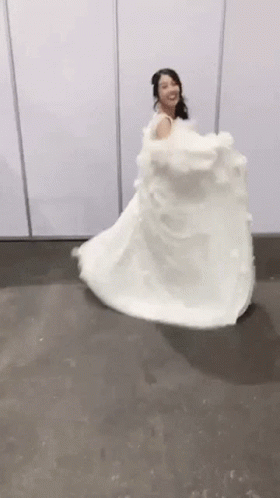 A Woman In A White Wedding Dress Is Dancing On A Floor . GIF